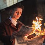 A man is reading newspaper confidently which is burning.